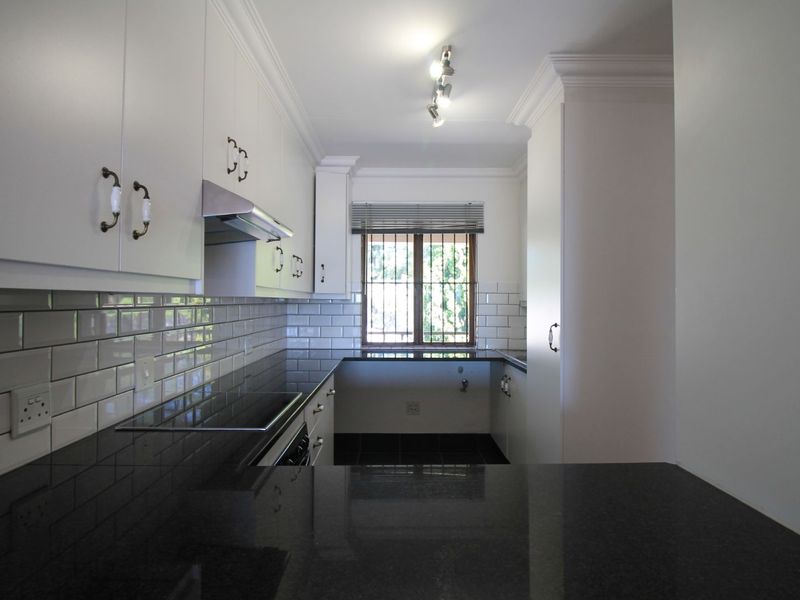 A clean, modern kitchen featuring white cabinetry, dark granite countertops, subway tile backsplash, and integrated appliances, offering a bright and functional workspace.