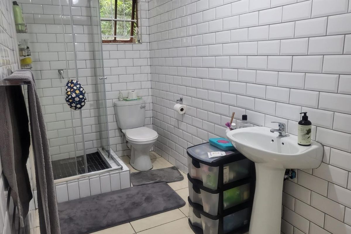 A functional bathroom featuring white subway wall tiles, a glass-enclosed shower, a pedestal sink, and a standard toilet.