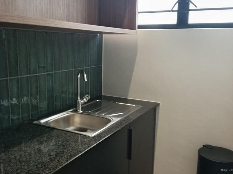 A modern, well-maintained scullery area featuring dark cabinetry, granite countertops, a stainless steel sink, and stylish green tiled backsplash.