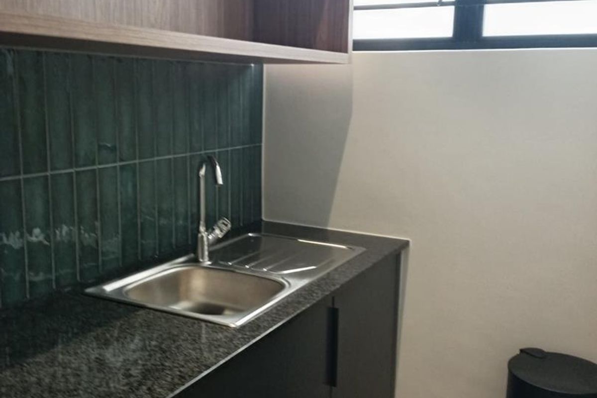 A modern, well-maintained scullery area featuring dark cabinetry, granite countertops, a stainless steel sink, and stylish green tiled backsplash.