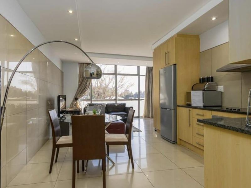 Modern open-plan living area featuring a functional kitchen with granite countertops, tiled flooring, and large glass doors leading to an outdoor space.