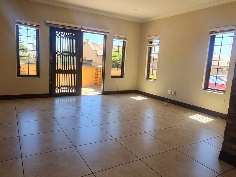 A spacious, empty living area featuring large tiled floors, neutral walls, and a sliding door leading to an outdoor patio area.