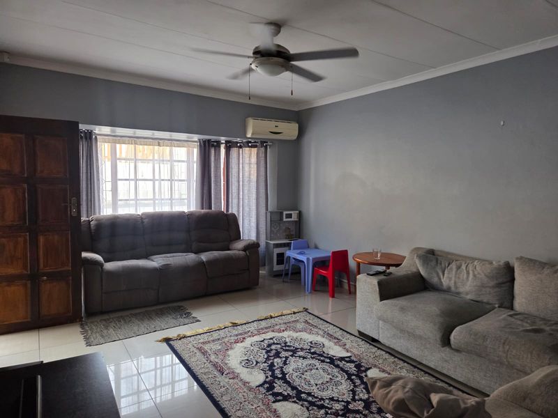 A spacious living room featuring tiled flooring, a ceiling fan, and a wall-mounted split system air conditioner.