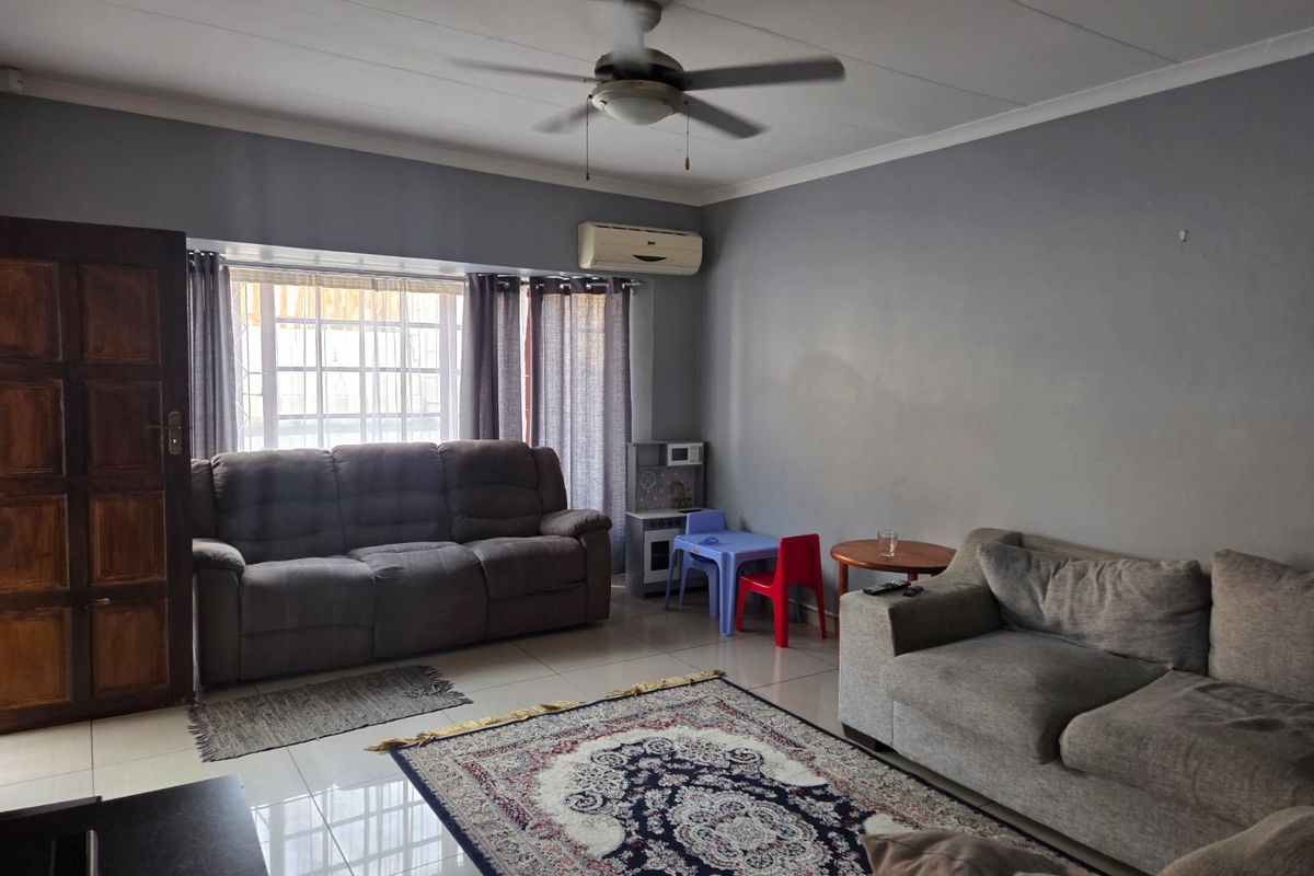 A spacious living room featuring tiled flooring, a ceiling fan, and a wall-mounted split system air conditioner.