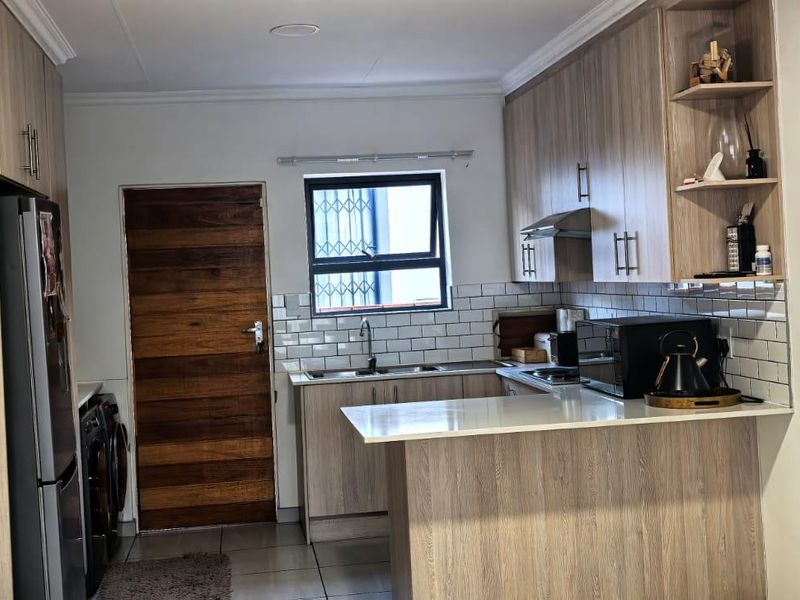 Modern kitchen featuring light wood-grain cabinetry, a subway tile backsplash, a functional breakfast bar, and a window with security bars.