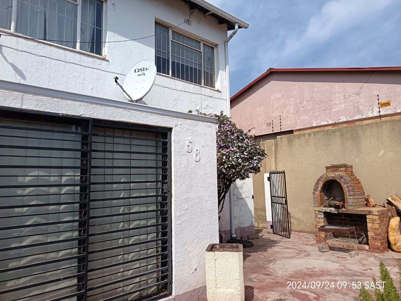 Rear exterior view of the townhouse featuring a built-in brick braai, paved courtyard area, and security gate access.