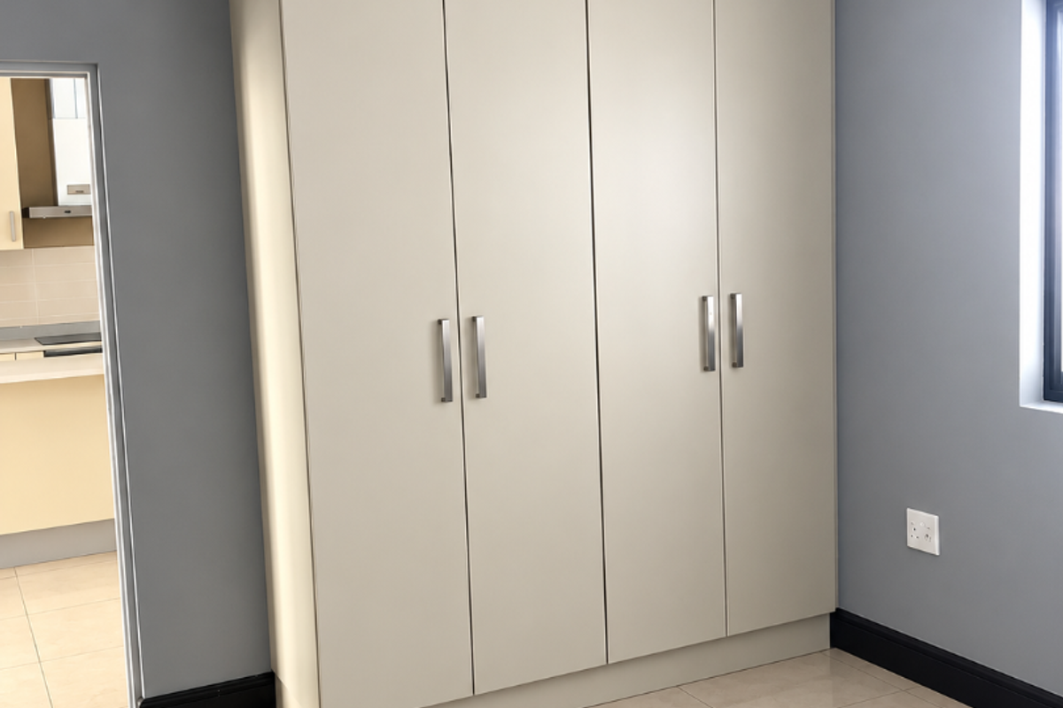 A clean, modern bedroom featuring neutral-toned built-in wardrobes, polished tile flooring, and grey walls with crisp white crown molding.