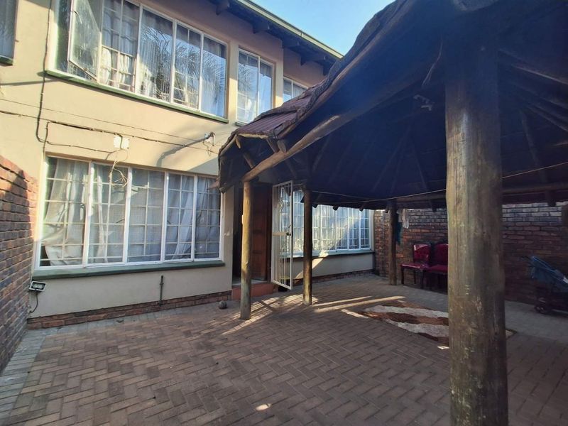 A paved outdoor patio area featuring a thatched lapa with timber support posts, enclosed by a brick boundary wall and overlooking the townhouse facade.