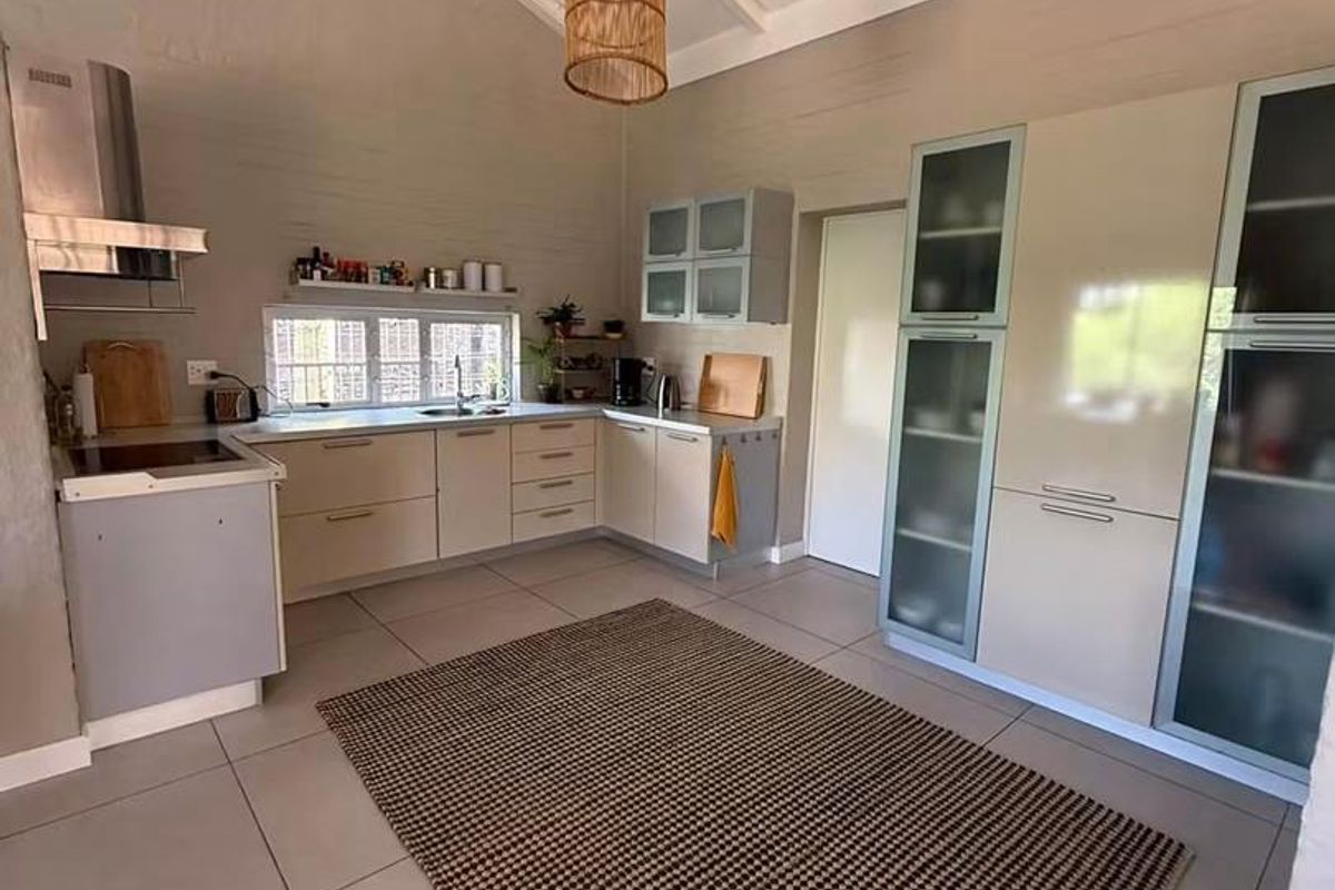 Modern kitchen featuring sleek built-in cabinetry, stainless steel extractor fan, tiled flooring, and an airy vaulted ceiling with exposed beams.