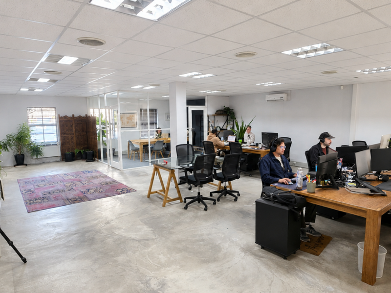 Spacious open-plan office area featuring polished concrete floors, suspended ceiling with recessed lighting, and a glass-partitioned meeting room.