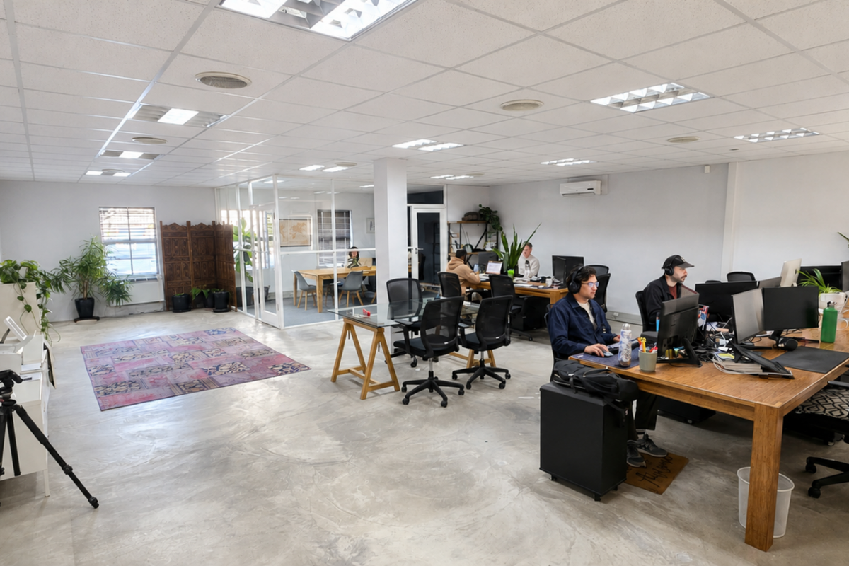 Spacious open-plan office area featuring polished concrete floors, suspended ceiling with recessed lighting, and a glass-partitioned meeting room.