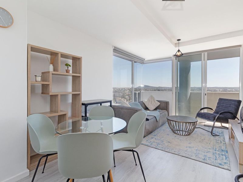 Bright open-plan living and dining area featuring floor-to-ceiling windows, sliding glass doors to the balcony, and modern laminate flooring with panoramic city views.