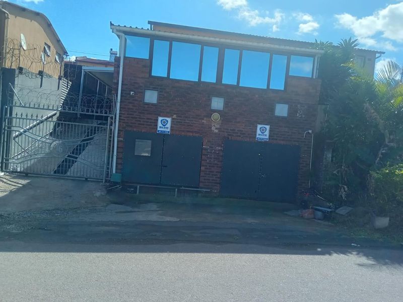 Front exterior view of a brick house featuring a double garage, security gate, and perimeter razor wire fencing.