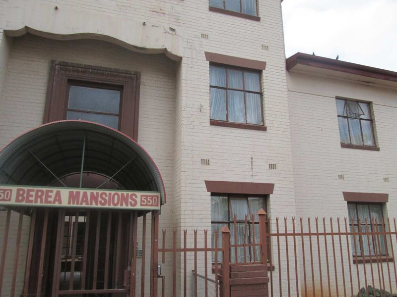 Front elevation of Berea Mansions apartment building featuring a brick facade, arched entrance canopy, and perimeter security fencing.