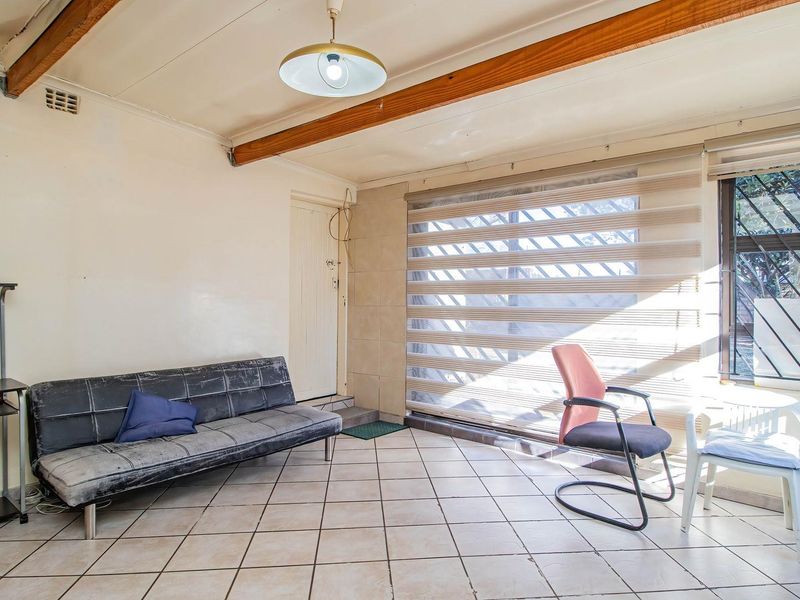 Living area featuring ceramic floor tiles, exposed timber ceiling beams, and large windows with security bars and roller blinds.