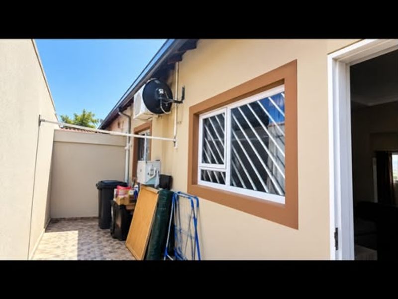 A view of the rear exterior area featuring tiled flooring, security bars on the window, and an external air conditioning unit.