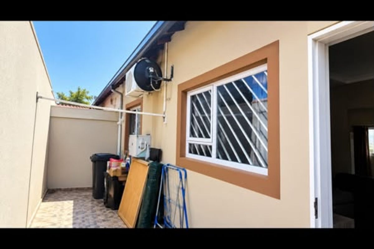 A view of the rear exterior area featuring tiled flooring, security bars on the window, and an external air conditioning unit.