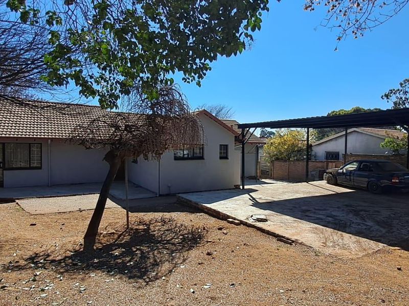 Rear view of the property featuring a tiled roof house, a metal carport structure, and a large open yard area.