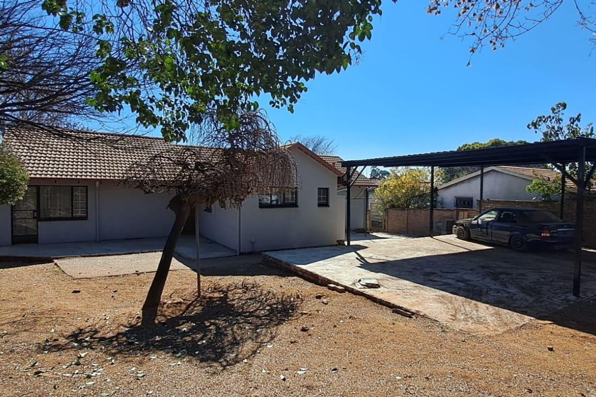 Rear view of the property featuring a tiled roof house, a metal carport structure, and a large open yard area.