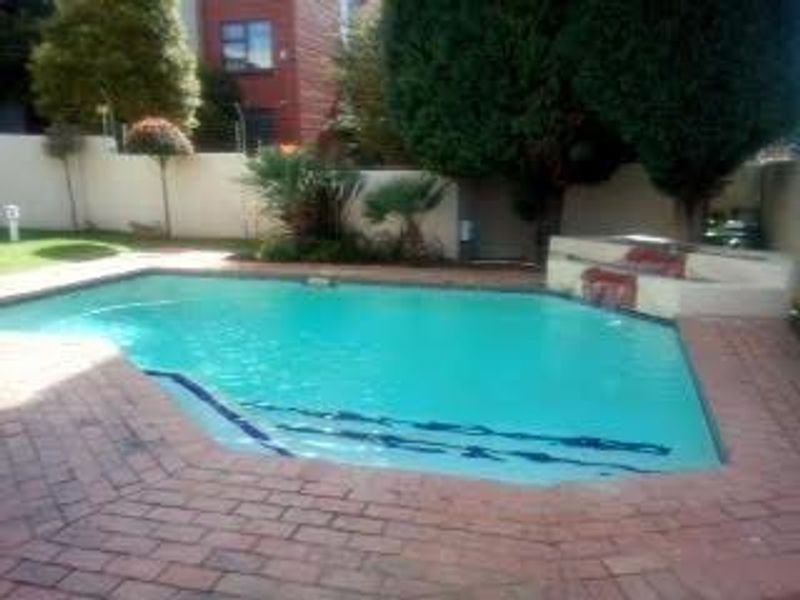Outdoor swimming pool area featuring brick paving, a built-in water feature, and surrounding landscaped garden elements.