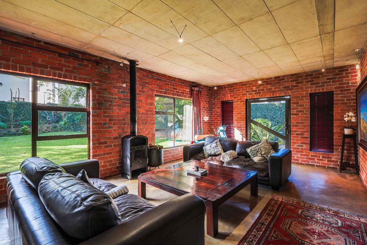 Spacious living room featuring exposed brick walls, concrete ceiling, and a built-in wood-burning fireplace with large windows overlooking the garden.