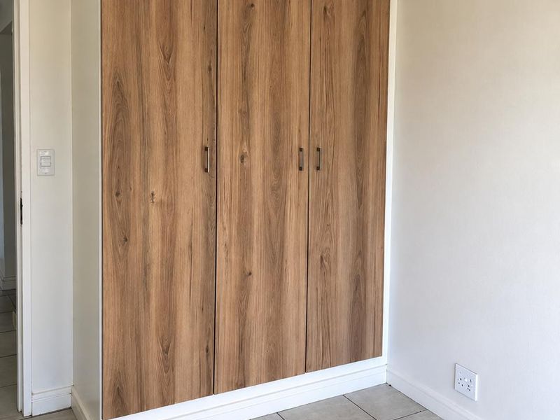 A clean, empty bedroom featuring modern wood-finish built-in wardrobes, neutral tiled flooring, and crisp white walls, offering a versatile space ready for personalization.