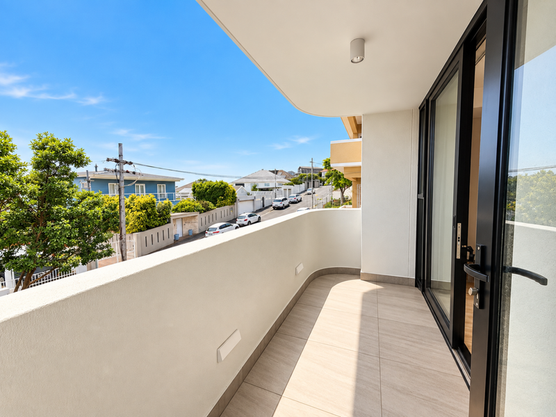 A clean, modern balcony featuring neutral floor tiles, a solid balustrade, and large sliding glass doors providing access to the apartment interior.