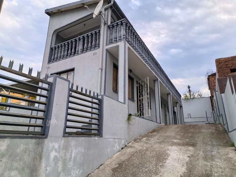 Two-story residential property featuring a concrete driveway, upper-level balcony with balustrade, and secure perimeter walling.
