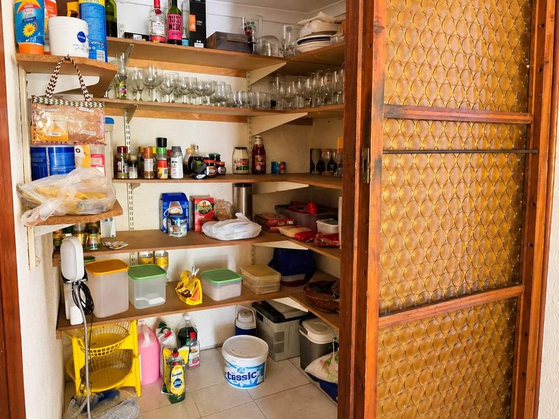 A functional walk-in pantry or scullery area featuring extensive built-in shelving and a sliding door with decorative textured glass.