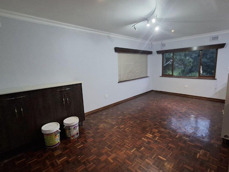 Spacious living area featuring classic parquet flooring, built-in cabinetry, and large windows with fitted blinds, offering a clean and neutral blank canvas.