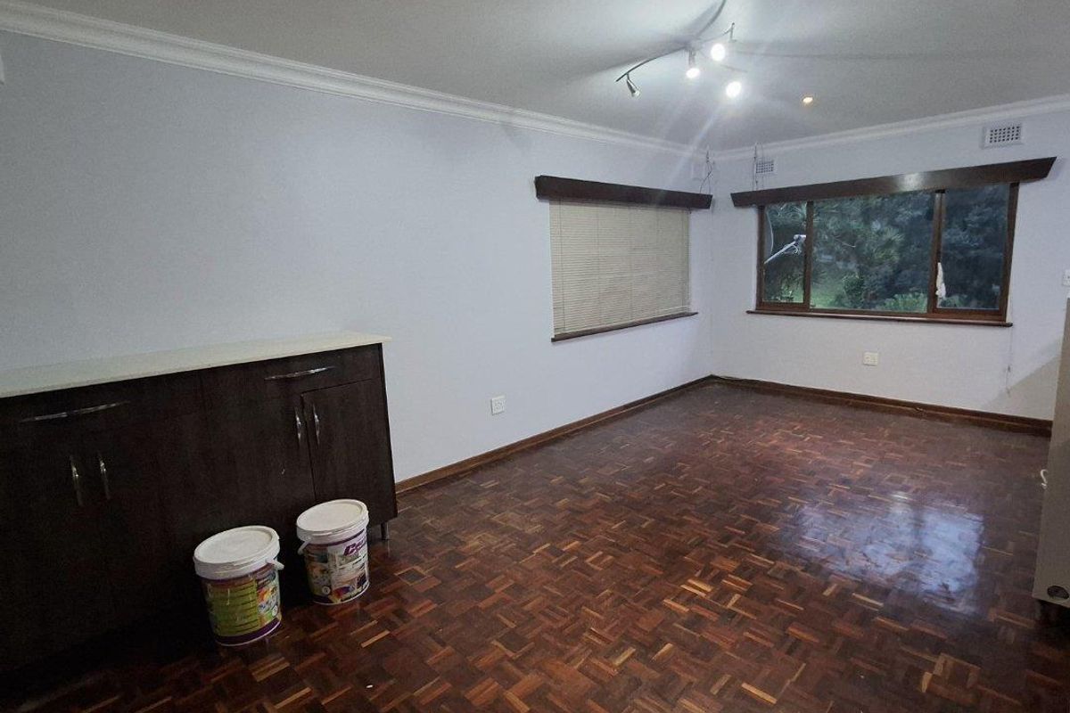 Spacious living area featuring classic parquet flooring, built-in cabinetry, and large windows with fitted blinds, offering a clean and neutral blank canvas.