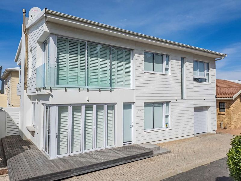 Modern two-story residential facade featuring white horizontal cladding, timber decking, glass balcony balustrades, and integrated garage access.