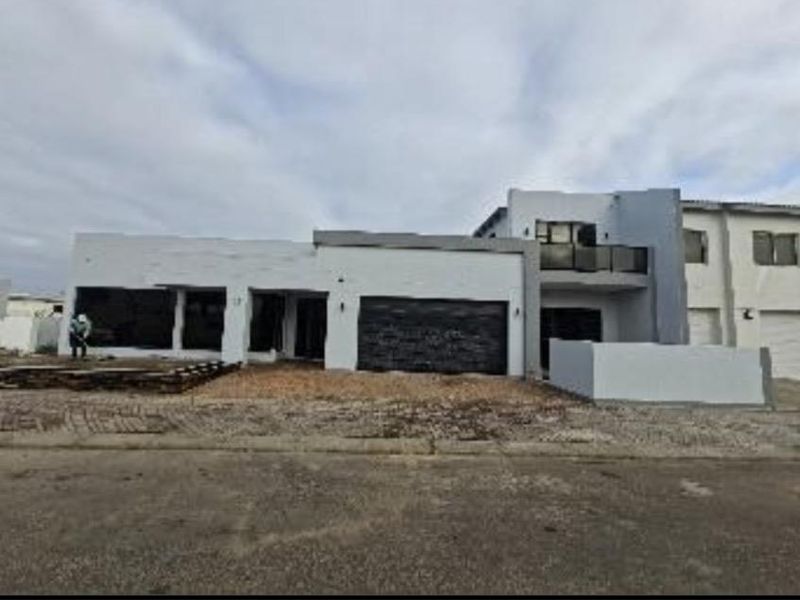 Front elevation of a modern double-story house featuring a double garage, balcony, and unfinished landscaping in a residential estate.