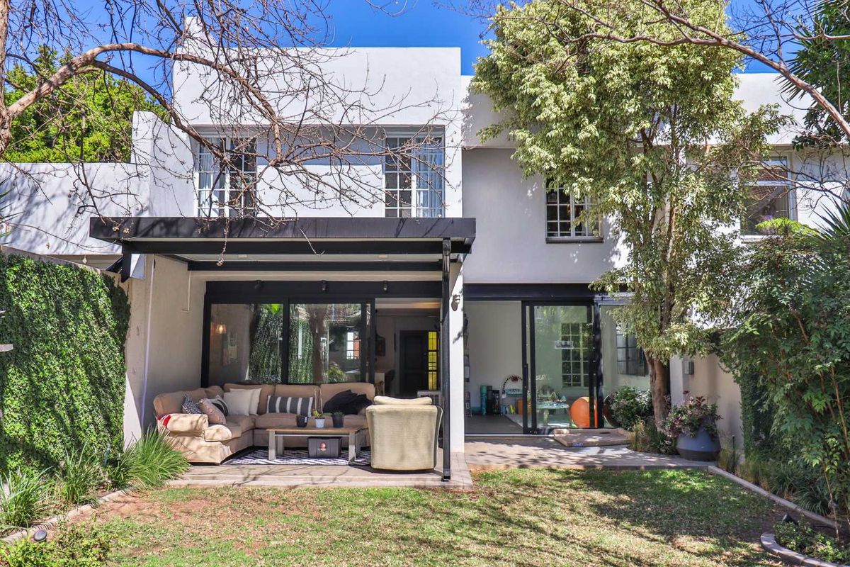Rear view of the townhouse featuring a covered patio area with sliding glass doors, leading into the living space, set against a private garden.
