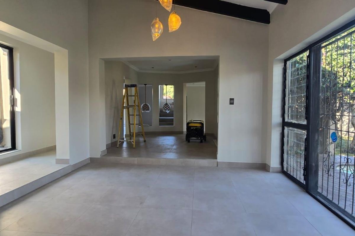 Spacious, light-filled living area featuring vaulted ceilings, neutral tiled flooring, and large sliding glass doors providing direct access to the garden.