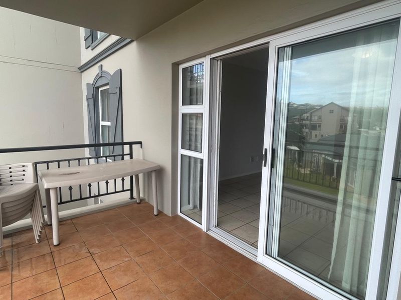 A covered balcony featuring tiled flooring, a metal balustrade, and sliding glass doors providing access to the interior living space.