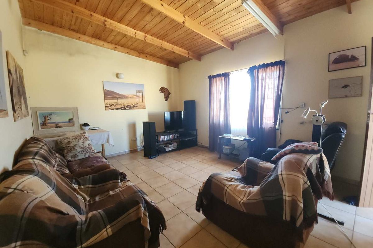 A living room featuring a high exposed timber beam ceiling and ceramic tiled flooring, offering a rustic aesthetic with potential for modernization.