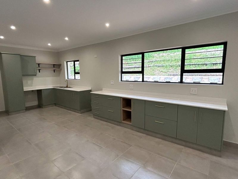 Modern, spacious kitchen featuring sage green cabinetry, stone countertops, tiled flooring, and ample natural light from large windows.