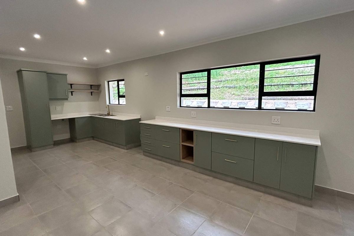 Modern, spacious kitchen featuring sage green cabinetry, stone countertops, tiled flooring, and ample natural light from large windows.