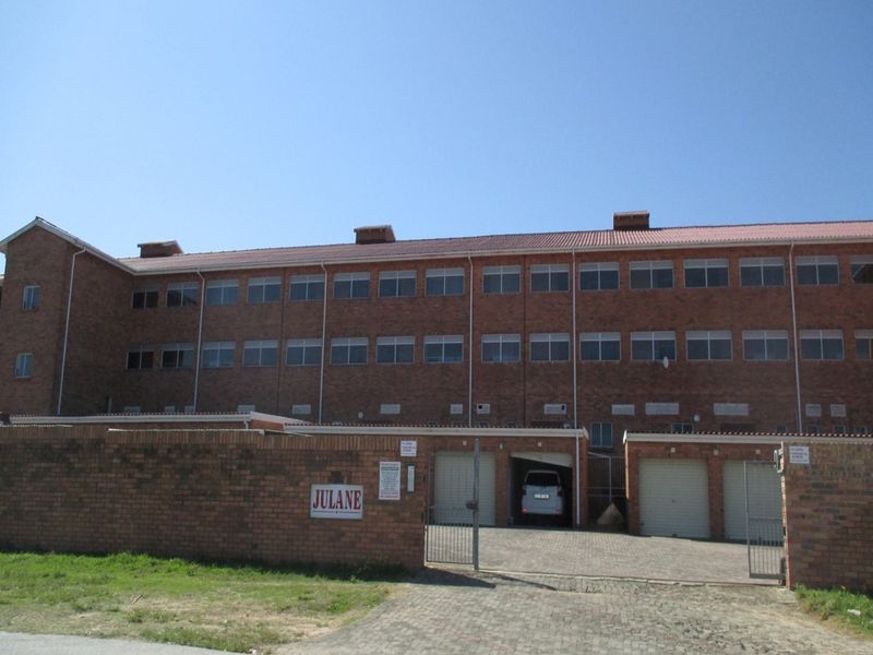 Front elevation of a multi-story brick apartment complex featuring a paved driveway, secure garage access, and perimeter walling.