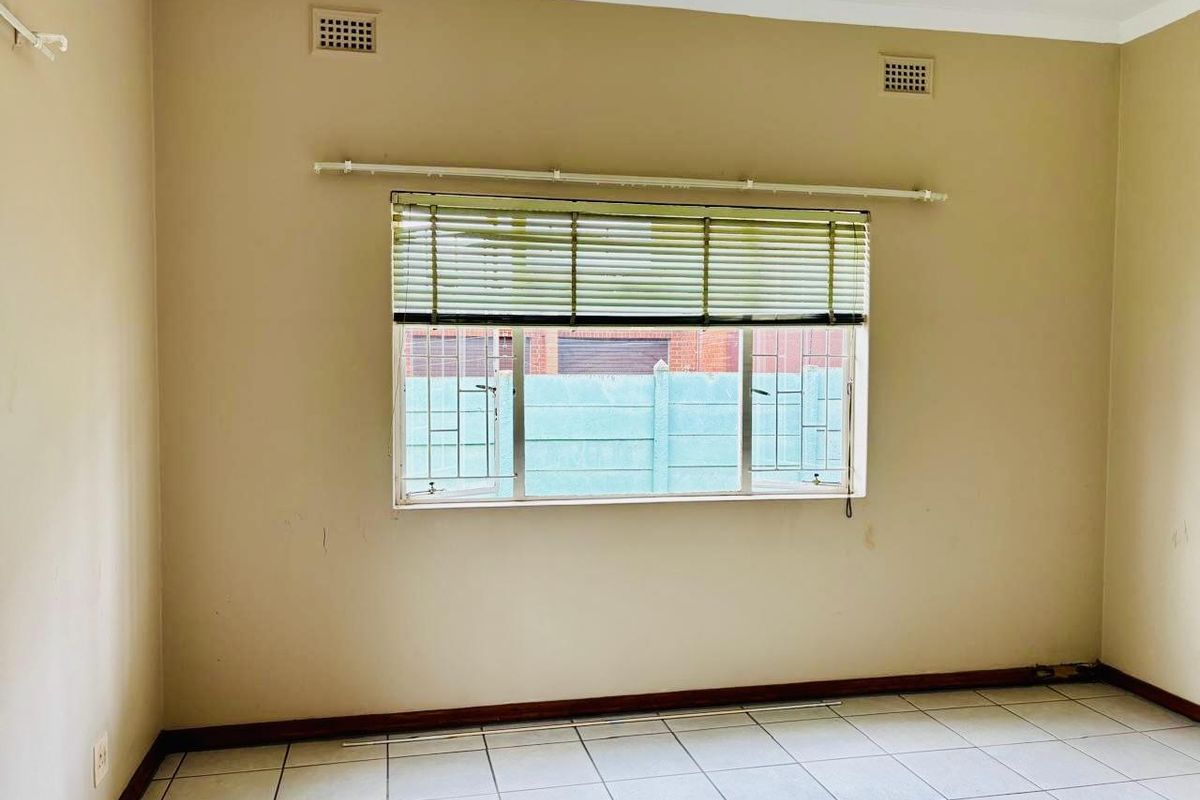 An empty bedroom featuring tiled flooring, a large window with fitted blinds, and dual ceiling ventilation grilles.