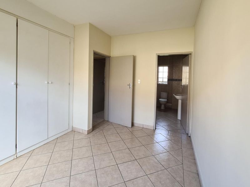 An empty bedroom featuring tiled flooring and built-in cupboards, with direct access to an en-suite bathroom.