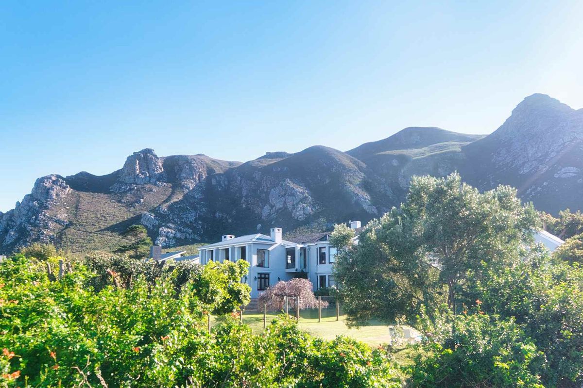 A scenic rear view of the property featuring a well-maintained garden and building facade set against a dramatic mountain backdrop.