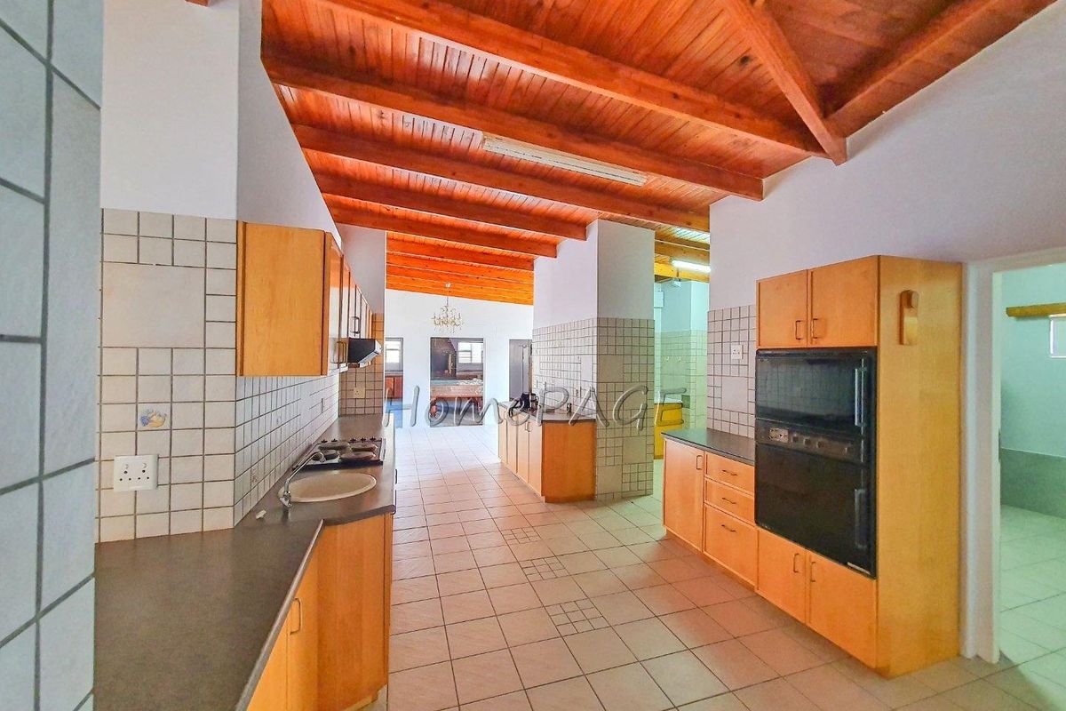 Spacious kitchen featuring wooden cabinetry, built-in oven, gas hob, and exposed timber beam ceiling, offering a functional layout with ample counter space.