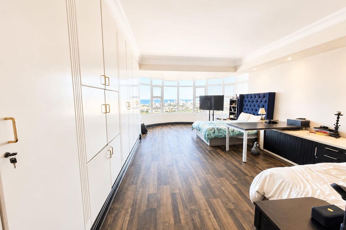 Spacious bedroom featuring extensive built-in cabinetry, laminate flooring, and a large bay window offering panoramic coastal views.