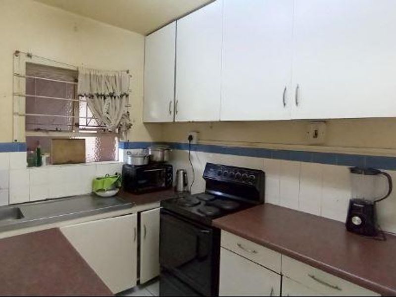 A functional kitchen featuring white built-in cabinetry, laminate countertops, a stainless steel sink, and an electric stove with a tiled backsplash.