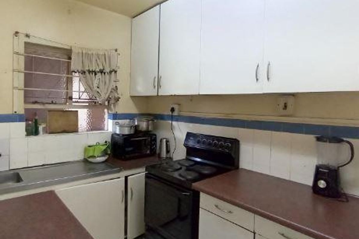 A functional kitchen featuring white built-in cabinetry, laminate countertops, a stainless steel sink, and an electric stove with a tiled backsplash.