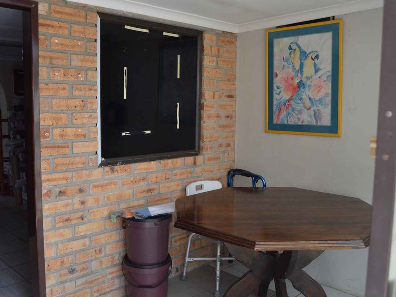 A covered patio area featuring exposed brickwork and tiled flooring, currently requiring maintenance to the window fixture.