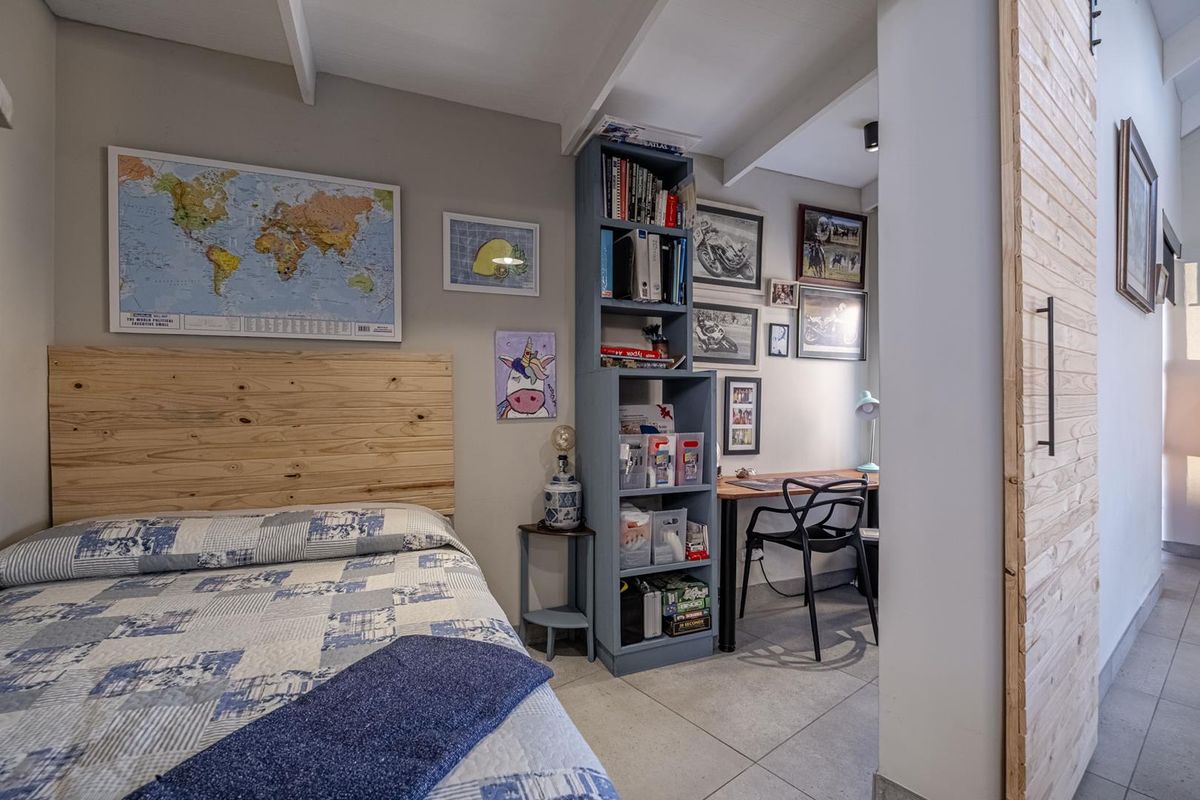 A well-maintained bedroom featuring tiled flooring, exposed beam ceiling, and a built-in wooden headboard, with an adjoining study nook area.