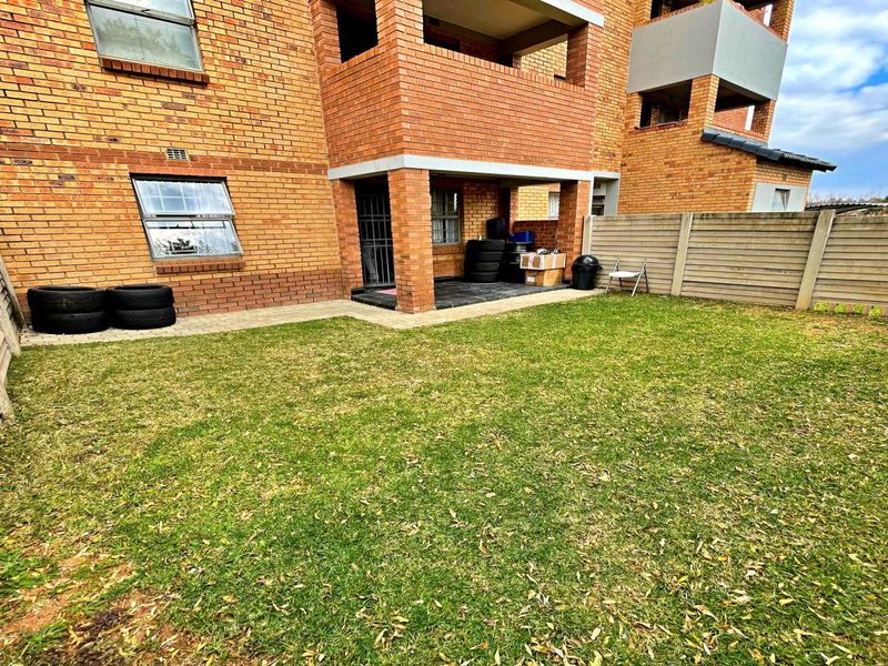 A private rear garden area featuring a lawn, precast concrete boundary walls, and a covered patio attached to the brick apartment building.